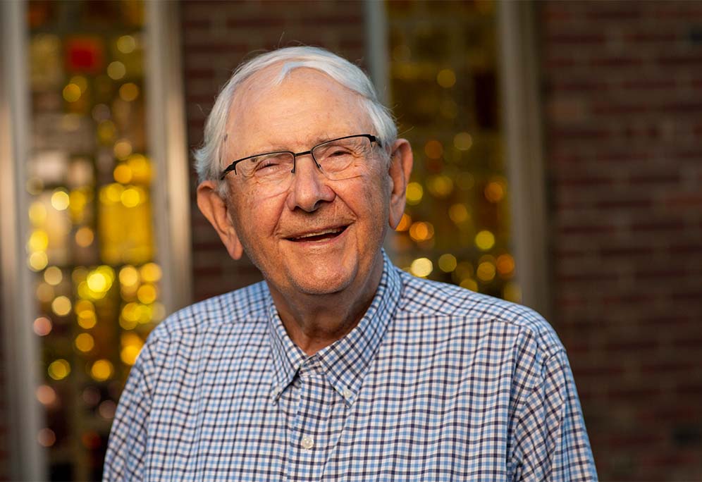 Closeup of Paul smiling and standing near a lit window